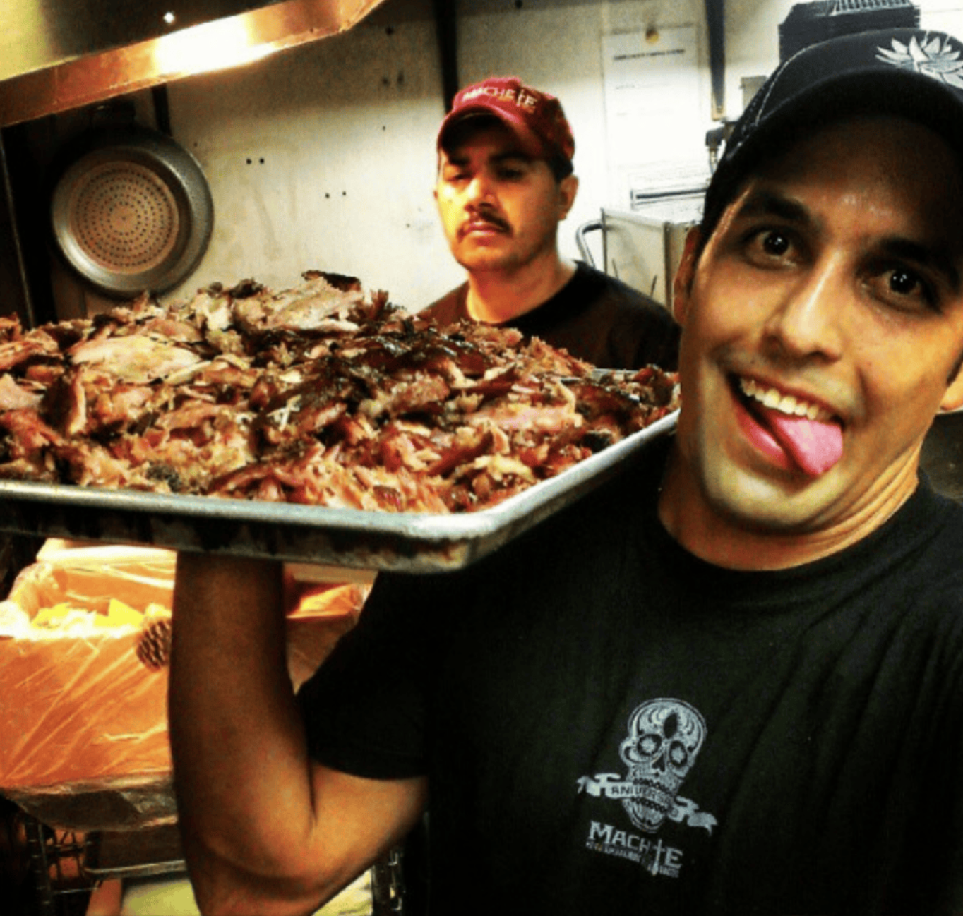 Man holding tray of cooked meat, smiling.